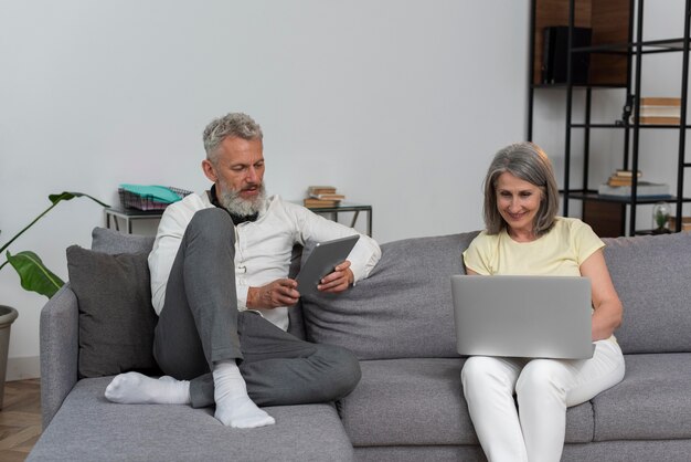 Hombre y mujer senior en casa en el sofá con laptop y tableta