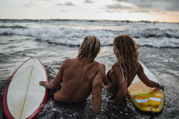 Hombre y mujer sentada en la playa con tablas de surf