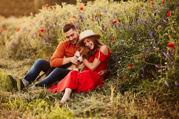 El hombre y la mujer se sientan con un Beagle divertido en el campo verde con amapolas rojas