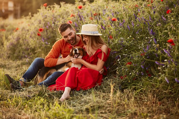 El hombre y la mujer se sientan con un Beagle divertido en el campo verde con amapolas rojas