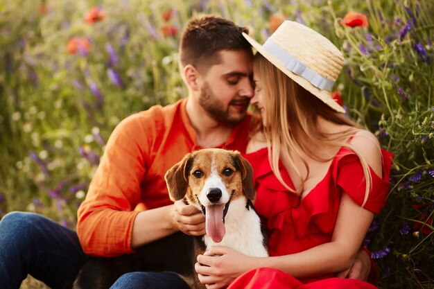 El hombre y la mujer se sientan con un Beagle divertido en el campo verde con amapolas rojas