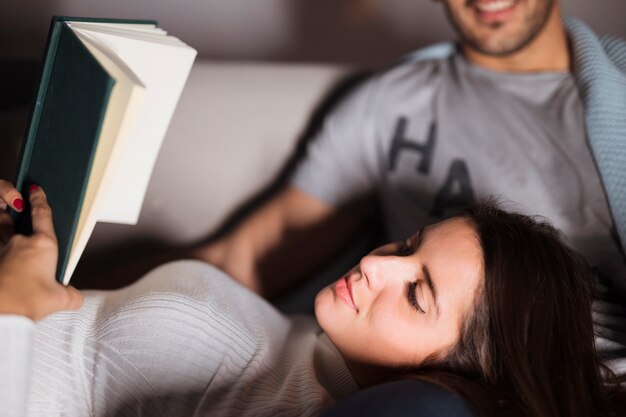 Hombre y mujer sonrientes jovenes con el libro en el sofá