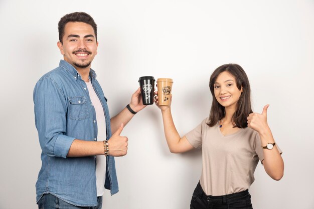 Hombre y mujer sonrientes con tazas de café y mostrando los pulgares para arriba.