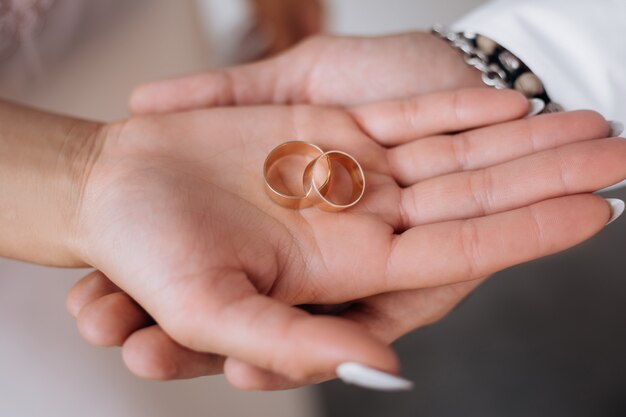 Hombre y mujer sostienen dos anillos de bodas de oro en sus brazos