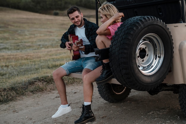 Hombre y mujer tocando la guitarra mientras viajan por care =