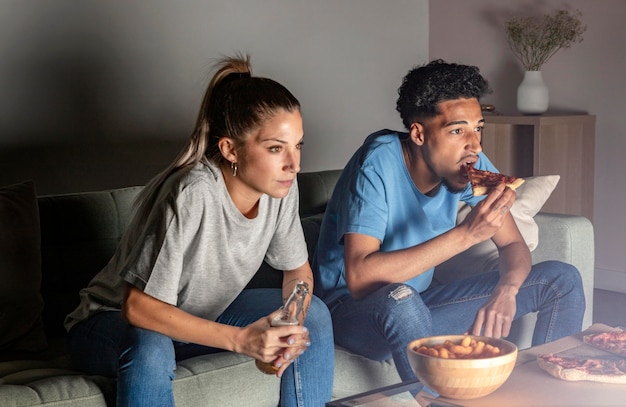 Hombre y mujer tomando cerveza y bocadillos en casa mientras ve la televisión