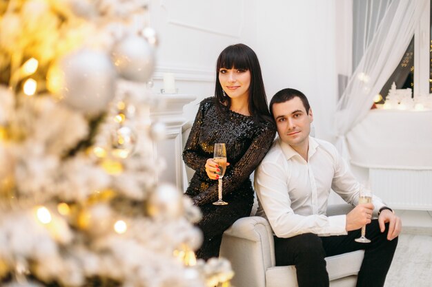 Hombre y mujer vestidos para una cena festiva frente a un brillante árbol de Navidad