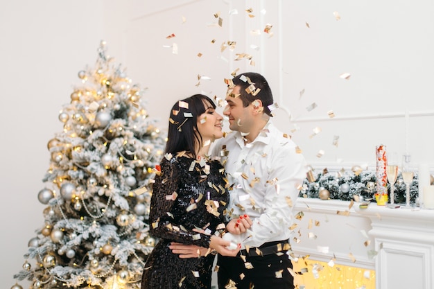 Hombre y mujer vestidos para una cena festiva frente a un brillante árbol de Navidad