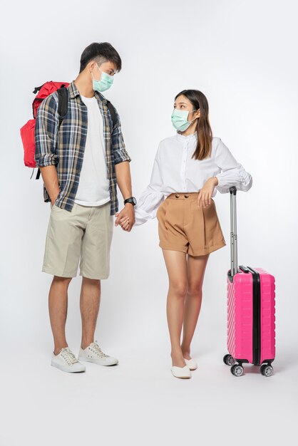 Hombre y mujer vestidos para viajar, con máscaras junto con el equipaje