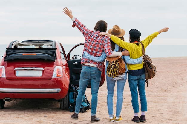 Hombre y mujeres abrazando cerca de coche en la costa del mar