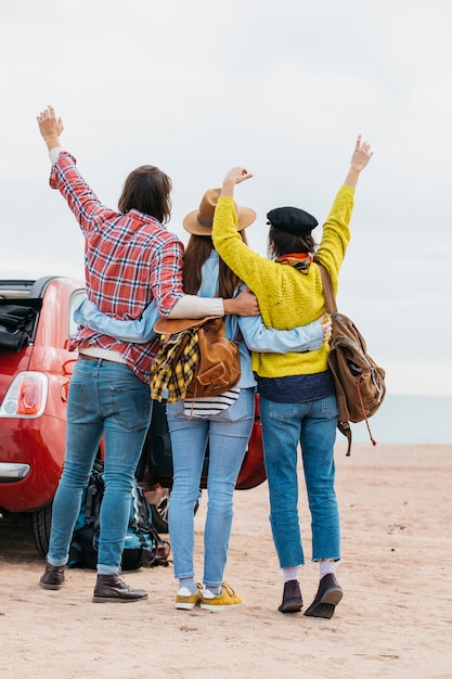 Foto gratuita hombre y mujeres abrazando cerca de coche en la playa del mar