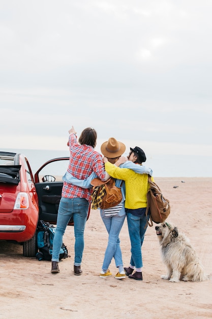 Foto gratuita hombre y mujeres abrazándose cerca de carro y perro en la playa del mar