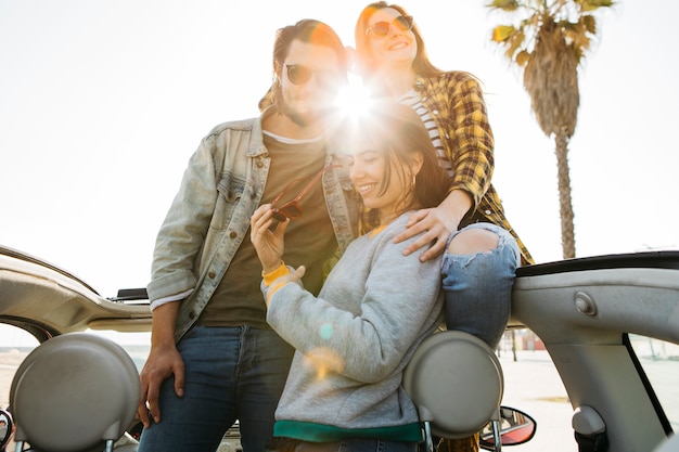 Hombre y mujeres alegres abrazándose e inclinándose fuera del auto