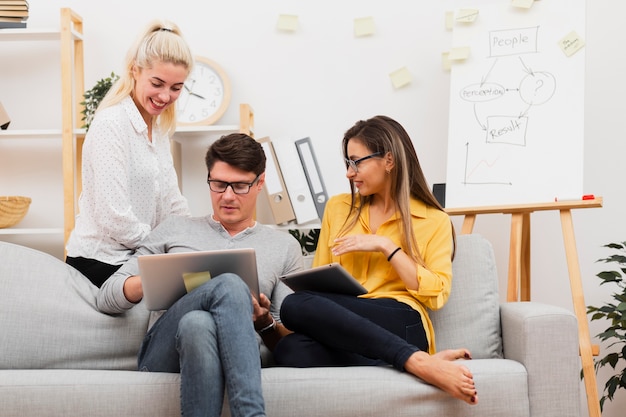 Hombre y mujeres sentados en el sofá y trabajando en la computadora portátil