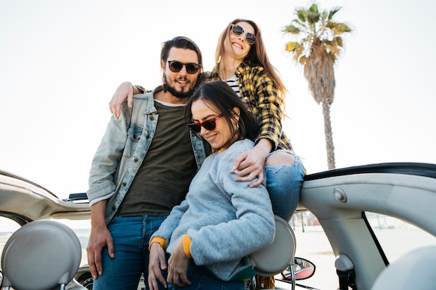 Foto gratuita hombre y mujeres sonrientes que abrazan y se inclinan hacia fuera del coche