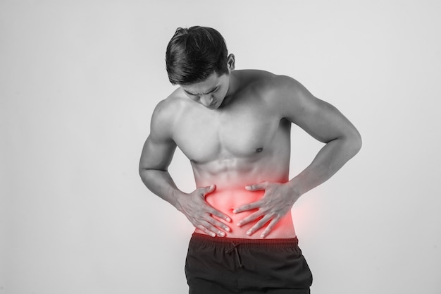 El hombre muscular hermoso joven tiene dolor abdominal aislado en el fondo blanco.