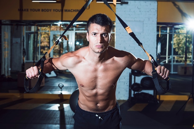 Hombre muscular que ejercita con la correa de la aptitud en gimnasio