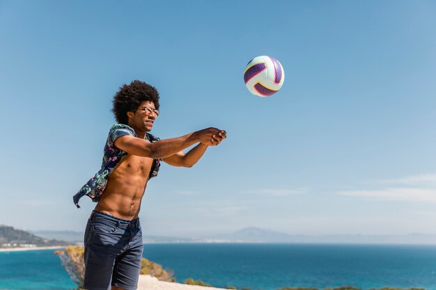 Hombre musculoso afroamericano saltando y sirviendo pelota