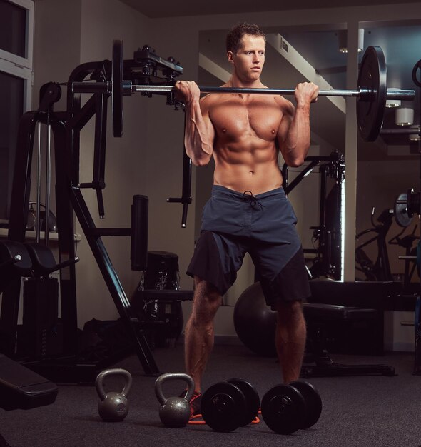 Hombre musculoso culturista sin camisa levantando una barra en un bíceps en el gimnasio.