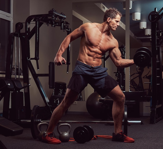 Hombre musculoso culturista haciendo ejercicios de bíceps con pesas en el gimnasio.