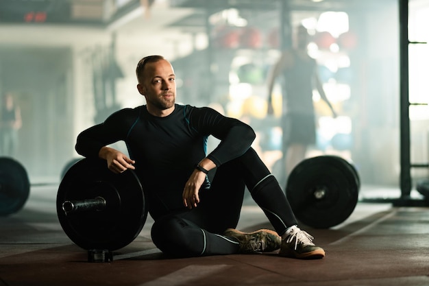 Foto gratuita hombre musculoso descansando después de un entrenamiento cruzado con pesas en un club de salud