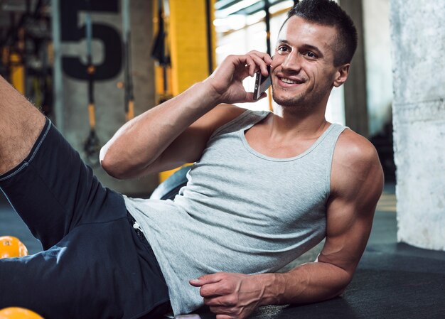 Hombre musculoso feliz hablando por celular en el gimnasio