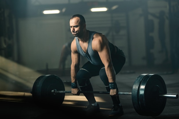 Hombre musculoso haciendo un esfuerzo mientras levanta pesas durante el entrenamiento cruzado en un gimnasio