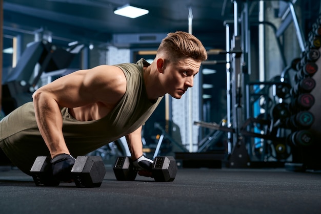 Hombre musculoso haciendo flexiones con pesas.