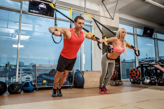 Hombre musculoso y mujer atlética haciendo ejercicios con expansor en un gimnasio.