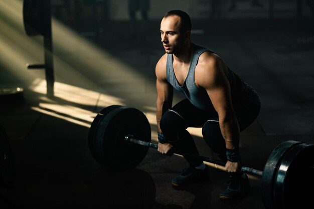Hombre musculoso realizando peso muerto mientras entrena con pesas en un gimnasio