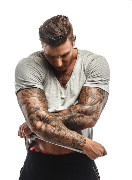 Foto gratuita hombre musculoso con tatuajes desnudándose. aislado en blanco