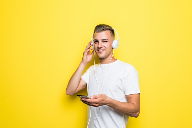 Hombre muy guapo en camiseta blanca escuchar música con sus nuevos auriculares aislados en la pared amarilla