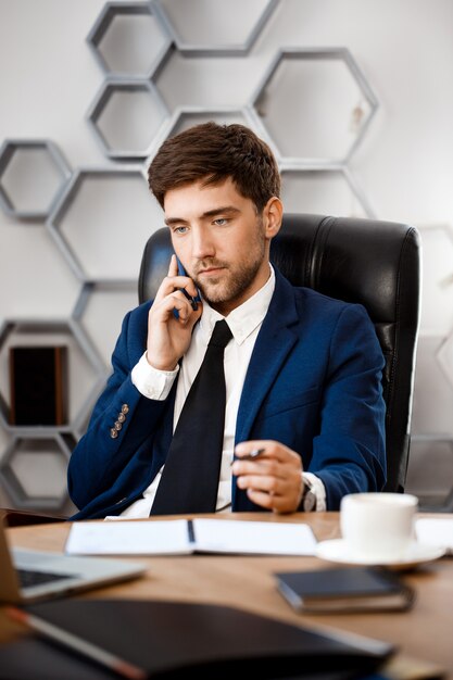 Hombre de negocios acertado joven que habla en el teléfono, fondo de la oficina.