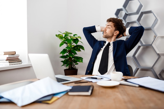 Foto gratuita hombre de negocios acertado joven que se sienta en el lugar de trabajo, fondo de la oficina.