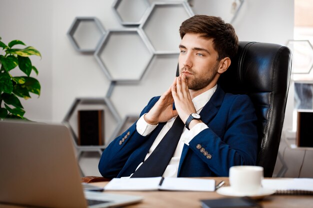 Hombre de negocios acertado joven que se sienta en el lugar de trabajo, fondo de la oficina.