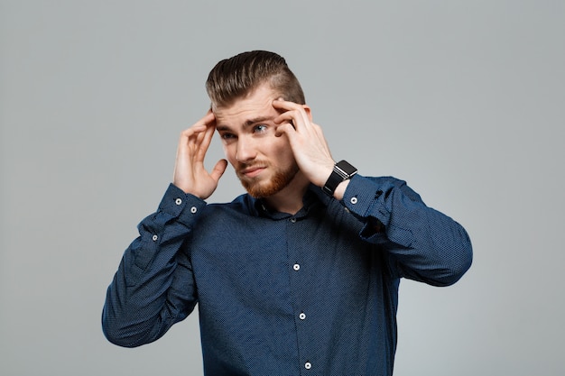 Hombre de negocios acertado joven que tiene dolor de cabeza sobre la pared gris.