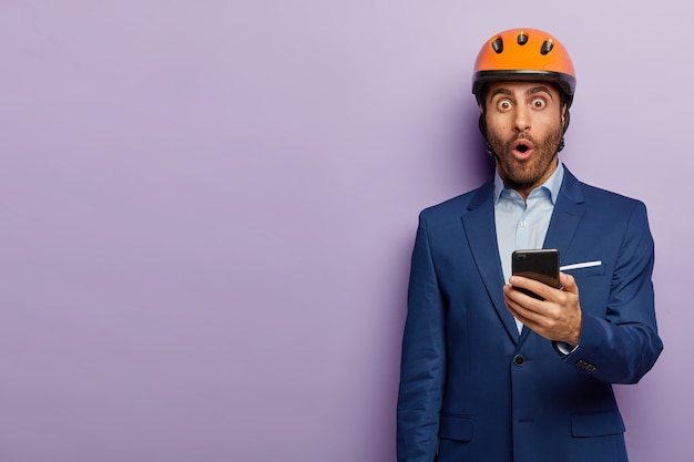 Hombre de negocios acertado que presenta en traje elegante y casco rojo en la oficina