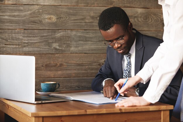 Hombre de negocios afroamericano concentrado comprobando papeles con su asistente personal en camisa blanca