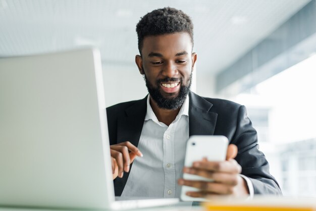 Hombre de negocios afroamericano joven que usa el teléfono y haciendo gesto ganador con el puño en la oficina