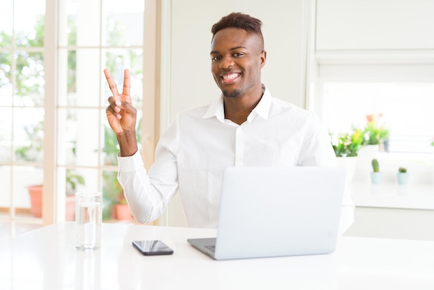 Foto gratuita hombre de negocios afroamericano que trabaja usando una computadora portátil sonriendo con cara feliz guiñando un ojo a la cámara haciendo el signo de la victoria número dos