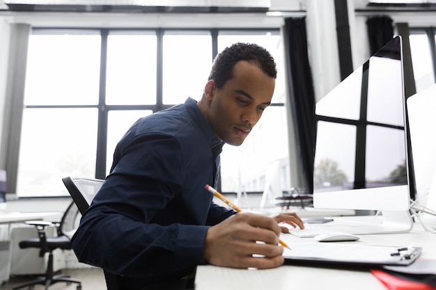 Hombre de negocios afroamericano tomando notas mientras está sentado en su escritorio