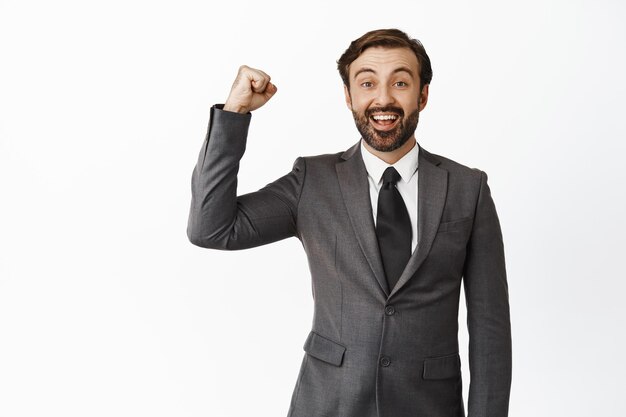 Un hombre de negocios alegre apoyando al equipo levantando el puño cerrado en apoyo sonriendo y mirando esperanzado a la cámara animando al equipo de pie sobre fondo blanco