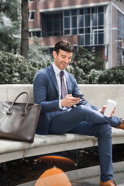 Foto gratuita hombre de negocios alegre con bebida navegación smartphone