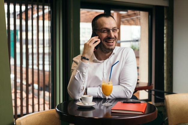 Hombre de negocios alegre hablando en teléfono inteligente en el café