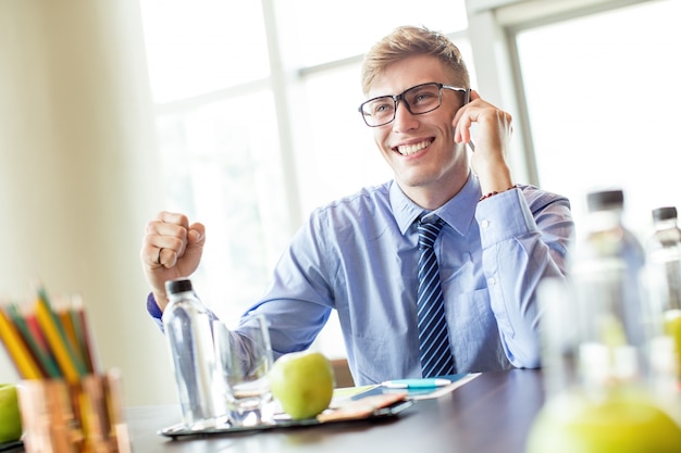 Foto gratuita hombre de negocios alegre hablando por teléfono en la mesa