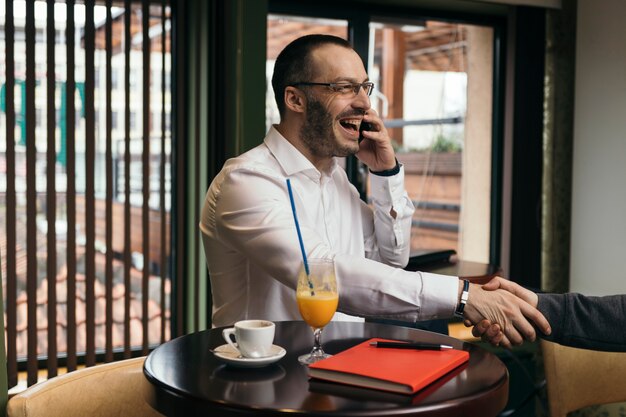 Hombre de negocios alegre que asiste en el teléfono y que sacude la mano