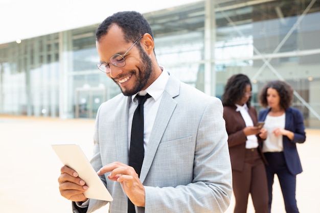 Hombre de negocios alegre que usa la tableta afuera