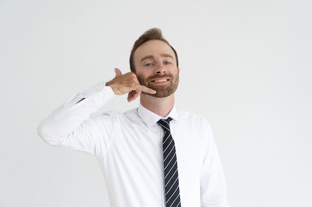 Hombre de negocios ampliamente sonriente que pide por gesto telefonearlo.