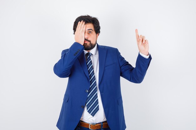 Hombre de negocios apuntando a la derecha con los dedos índices y cubriendo los ojos con traje formal y mirando serio. vista frontal.