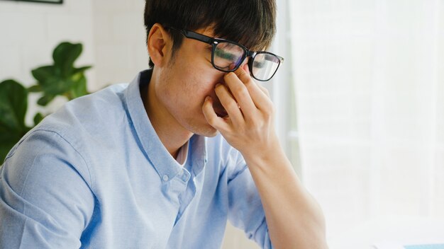 Hombre de negocios de Asia usando laptop está molesto por el trabajo, rasgando papeles y gritando en la sala de estar en casa. Trabajo desde casa, trabajo a distancia, distanciamiento social, cuarentena para la prevención del virus corona.